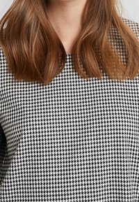 Černobílý top s vzorem houndstooth a kulatým výstřihem, vyrobený z texturovaného materiálu a s mírně volným střihem.