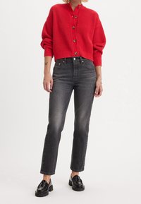 Cardigan de punto acanalado rojo con botones en la parte frontal, combinado con jeans de denim gris de talle alto y mocasines negros. Diseño simple y casual.