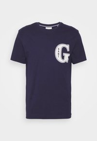 Camiseta de algodón de cuello redondo en azul marino con el logo blanco "GANT G" en el lado izquierdo del pecho. Mangas cortas y textura suave.