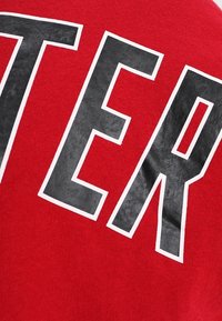 Felpa rossa con scritte nere in grassetto. Tessuto morbido, scollatura rotonda, maniche corte, con contorni bianchi attorno alle lettere. Il testo recita "SWEATER."