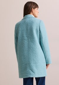 Cappotto di lana testurizzato blu chiaro con design di lunghezza media, colletto oversize e maniche lunghe. La vista posteriore mostra le cuciture e il tessuto morbido.