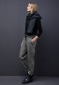 Pantalons cargo texturés gris avec poches latérales, associés à un pull noir et à une écharpe sombre, portés avec des bottines noires.
