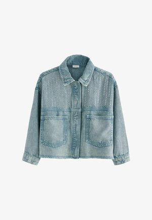 Kék farmerdzseki díszes szegecsekkel, világoskék színben, oversized szabásban, hozzáillő farmer szoknyával párosítva. Fekete pántos szandálban viselve.