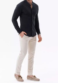 Camicia button-up a maniche lunghe di colore nero, pantaloni slim-fit di colore crema, mocassini marrone chiaro, design semplice, tessuto liscio e senza motivi visibili.