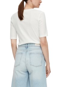 Korte mouwen witte katoenen t-shirt gecombineerd met lichtblauwe high-waisted denim broek met achterzakken en een losse pasvorm.