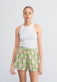 Top sans manches blanc avec col rond, associé à un short vert à motifs avec des fleurs roses et un design en zigzag, taille élastique et cordon de serrage.