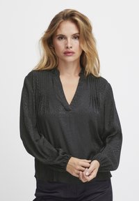 Blusa nera a maniche lunghe con scollatura a V e polsini arricciati. Tessuto con un motivo testurizzato, presentante dettagli sottili lungo il centro.