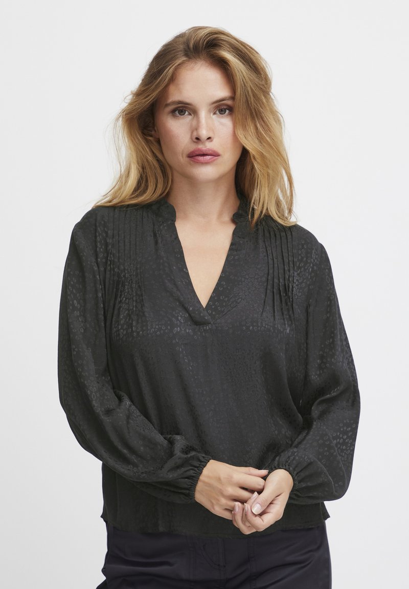 Blusa nera a maniche lunghe con scollatura a V e polsini arricciati. Tessuto con un motivo testurizzato, presentante dettagli sottili lungo il centro.
