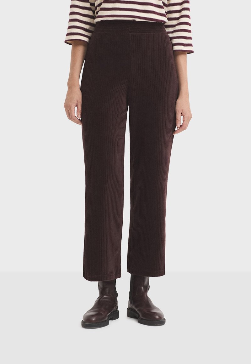 Woman wearing dark brown ribbed wide-leg pants, brown leather ankle boots, and a white and burgundy striped shirt with three-quarter sleeves.