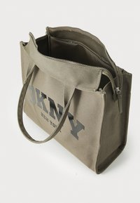 Sac en toile de couleur olive avec fermeture éclair, présentant un texte en relief gris "DKNY NEW YORK" et des poignées de transport doubles. L'intérieur est doublé.