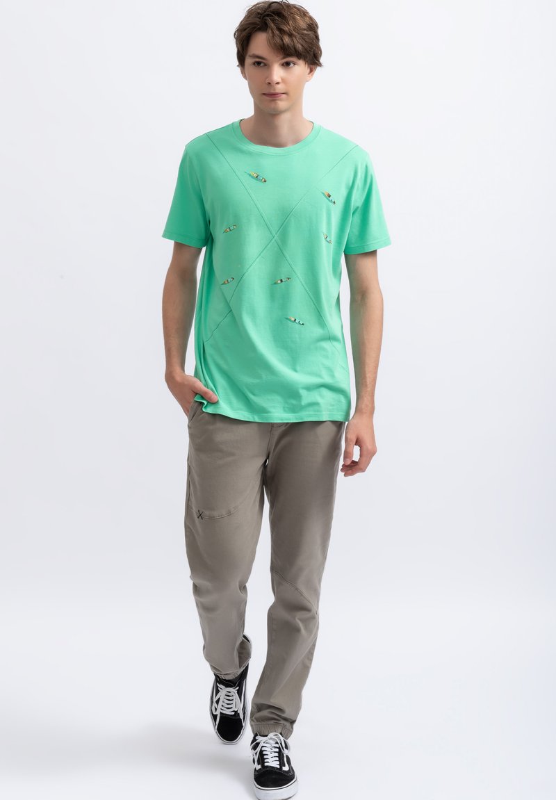 Lichtgroene katoenen t-shirt met diagonale naden en acht kleine decoratieve details. Gecombineerd met beige broek en zwarte sneakers.