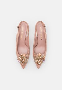 Rozā zamšādas slingback kedas ar asu purngalu, rotātas ar ziedu aplikāciju, kas izceļas ar daudzkrāsainiem akmeņiem un zelta akcentiem.