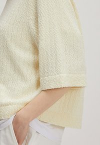 Kurzarmpullover in Creme mit strukturiertem Strickmuster. Der Stoff ist weich und leicht gerippt, verfügt über eine lockere Passform und umgeschlagene Bündchen.