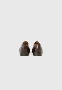 Zapatos de cuero marrón con una textura suave y punta redondeada. El tacón es negro con un ligero brillo. Presenta un patrón sutil a lo largo de los lados.