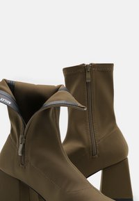 Brązowe botki za kostkę wykonane z gładkiej, elastycznej tkaniny. Posiadają masywny bloczek, boczny zamek oraz podwinięty kołnierz. Wykończone kontrastującym przeszyciem.