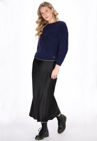 Marineblauwe fluffy trui met een ronde hals, gecombineerd met een zwarte satijnen midi rok en zwarte veterschoenen. Zilveren afwerking aan de zoom van de trui.