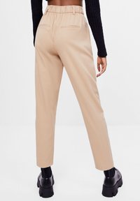 Beiga byxor med resårmidja, smalnande ben och två bakfickor. Bärs med svarta ankelstövlar och svarta texturerade långärmade tröjor.