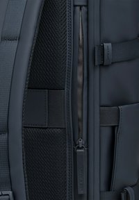 Intérieur d'un sac à dos bleu marine comprenant une poche en mesh, un tissu lisse, un compartiment à fermeture éclair, des matériaux bicolores et des détails de bretelles réglables.