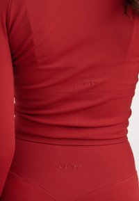 Gros plan sur le torse d'une personne portant un haut et un bas côtelés rouges assortis avec des logos "aim'n" subtilement embossés sur les deux vêtements.