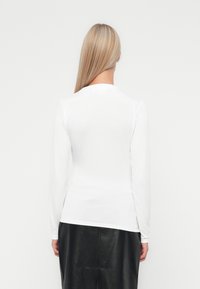 Witte blouse met lange mouwen en een aansluitende pasvorm, gladde textuur en een ronde halslijn, gedragen met een zwarte leren rok.