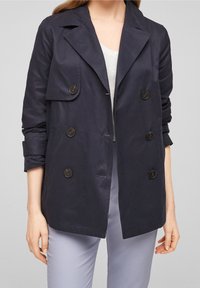Granatowy, dwurzędowy płaszcz trench z wywijanym kołnierzem, z dużymi guzikami i podwiniętymi rękawami, wykonany z gładkiego materiału.