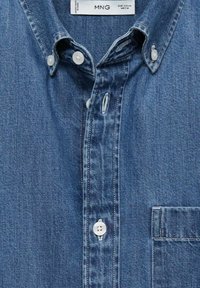 Camicia di denim blu medio con colletto button-down, bottoni bianchi, taschino sul petto e una texture morbida. Presenta striature sottili.