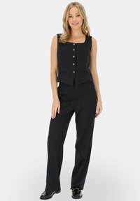 Granatowy garnitur w paski, który zawiera bezrękawnik o dopasowanym kroju z kwadratowym dekoltem i zapięciem na guziki z przodu, w połączeniu z szerokimi spodniami.