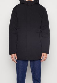 Abrigo negro, aislante, con capucha, cierre frontal de cremallera y dos bolsillos laterales. Presenta un diseño sencillo y recto, con una textura suave.