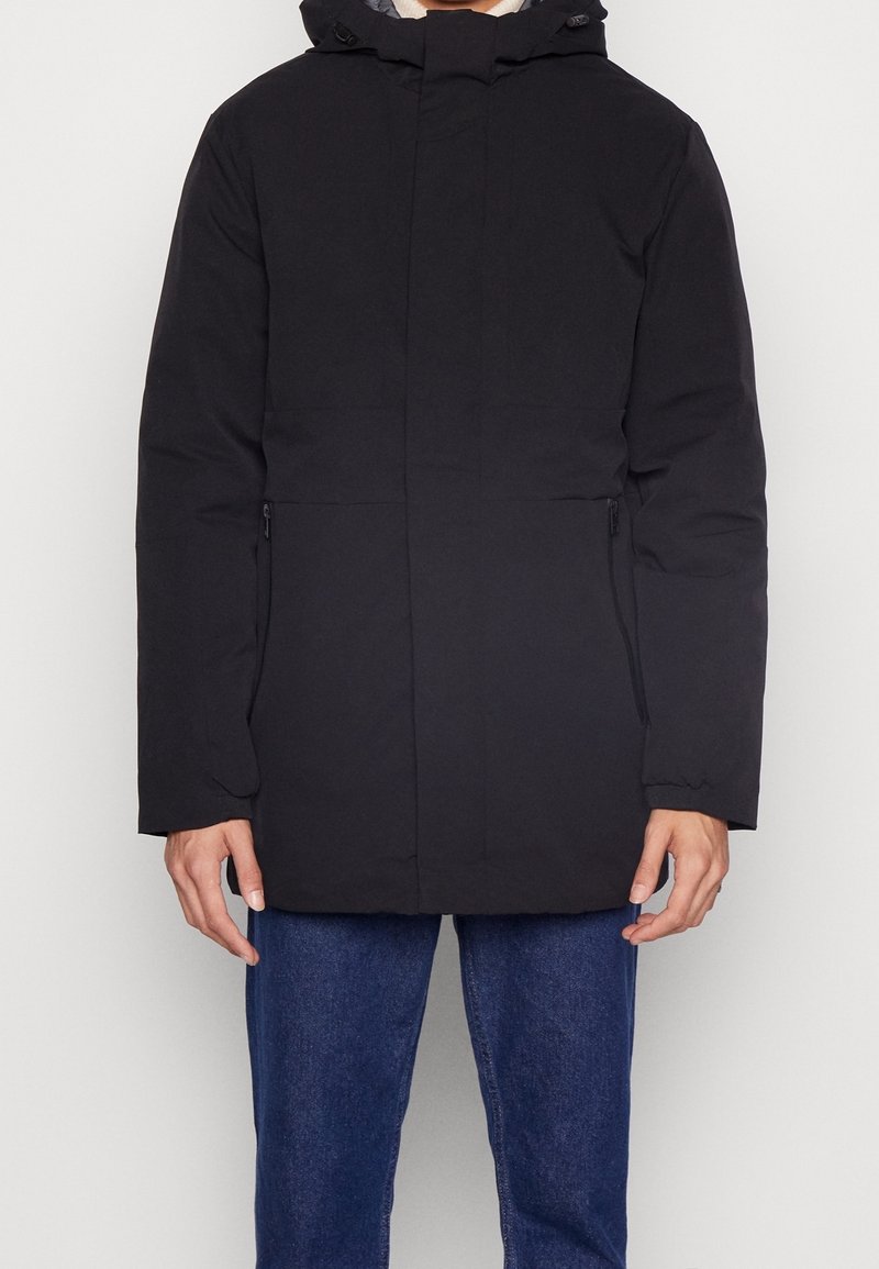 Abrigo negro, aislante, con capucha, cierre frontal de cremallera y dos bolsillos laterales. Presenta un diseño sencillo y recto, con una textura suave.