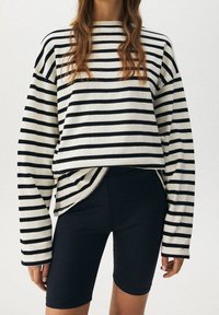 Czarny i biały pulower w paski z szerokim dekoltem i opadającymi ramionami, połączony z czarnymi szortami rowerowymi. Materiał mieszankowy bawełny.
