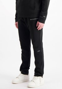 Zwarte sportbroek van een gladde stof, met een slim fit, subtiele stikdetails en een klein logo op de bovenkant van de dij.