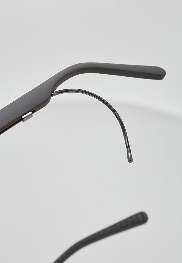 Gafas de sol negras con un diseño moderno y elegante, que cuentan con varillas planas y un brazo texturizado y flexible; acabado mate con una curvatura sutil.