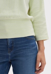 Pullover a righe verde chiaro realizzato in tessuto testurizzato, abbinato a jeans in denim blu scuro. Caratterizzato da una vestibilità comoda e maniche a tre quarti.