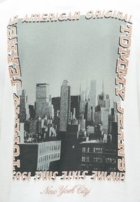Camiseta blanca con un diseño de horizonte en monocromo, texto "TOMMY JEANS" y la inscripción "New York City", con acentos de color contrastantes.