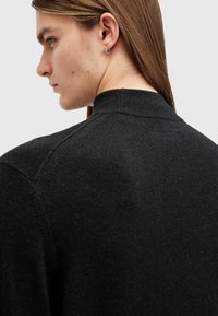 Maglione nero lavorato a maglia con colletto alto, caratterizzato da una finitura testurizzata e maniche raglan, parte di un design aderente.