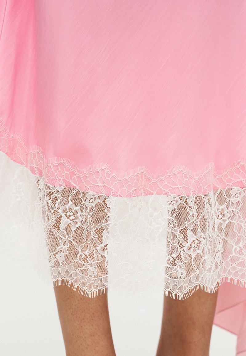 Robe rose à texture lisse, avec un bord en dentelle blanche à l'ourlet, présentant des motifs floraux complexes.