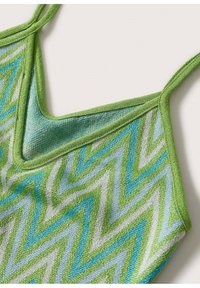 Top en tricot vert à motif zigzag avec des bretelles spaghetti ajustables. Il présente un décolleté en V et mélange des nuances de bleu et de vert.