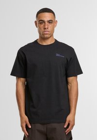 Černé bavlněné tričko s kulatým výst�řihem a krátkými rukávy, s malým modrým logem "HALO 19681972198" na hrudi.