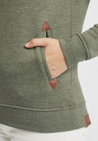 Maglione verde con tasca a canguro, dettagli triangolari marroni e finitura testurizzata, che mette in mostra un design aderente.