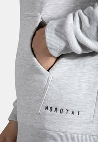 Felpa grigia con polsini a costine, una tasca laterale e ricamo "Morotai" in nero; texture morbida e design casual.