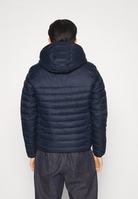 Mörkblå vadderad jacka med stor huva, quiltad design och elastiska muddar. Synliga sömmar och en kontrasterande tygdetalj på ärmen.