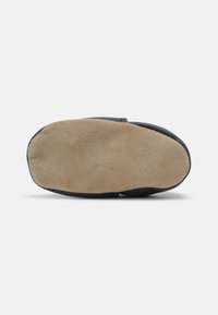 Pantofole nere con suola morbida in suede, caratterizzate da una tomaia liscia e un design con punta rotonda. La suola è prevalentemente beige.