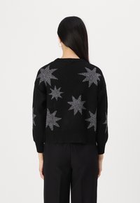 Black sweater with silver star patterns, featuring a round neckline and ribbed cuffs. The fabric appears soft and textured.