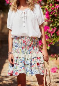 White, loose-fitting blouse with a tie neckline, paired with a multicolored floral skirt featuring ruffles and lace accents.