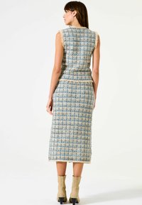 Blau- und cremefarbener Tweed-Kleid ohne Ärmel mit taillierter Form, Fransenverzierung und Midi-Länge, getragen mit beigen Stiefeletten.