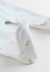 Ensemble bébé en coton blanc avec des motifs d'animaux jaune clair, comprenant des canards et des lapins, présentant des textures douces et des fermetures à pression.