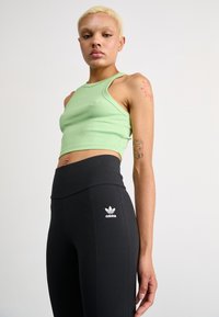 Zaļa ribota kroptopa no elastīga auduma, kas kombinēta ar augsto jostasvietu melnajām legingām ar baltu Adidas logo sānos.