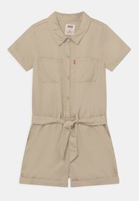 Beżowy kombinezon z krótkim rękawem, kołnierzykiem, dwiema kieszeniami na piersi, paskiem w talii oraz podwiniętymi mankietami. Wykonany z gładkiego materiału.