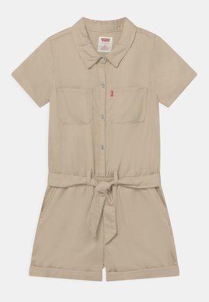 Combinaison beige à manches courtes avec un col, deux poches poitrine, une ceinture à la taille et des poignets retroussés. Fabriquée en tissu lisse.