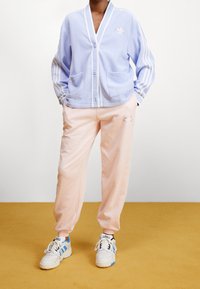 Light blue fleece cardigan with white trim and two pockets, paired with soft pink sweatpants featuring an embroidered design. White sneakers.